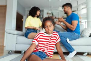 Upset kid daughter feels sad of parents fighting quarreling looking at camera, sad little mixed race girl frustrated with mom and dad arguing about child custody, family conflicts photo