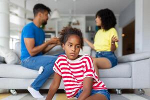Divorce And Domestic Violence. Portrait of upset African American daughter looking through the window while her angry parents fighting in the background, depressed child feeling lonely photo