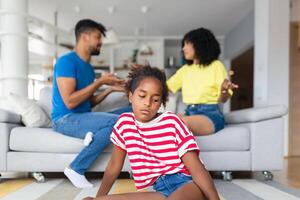 triste pequeño niña es mirando lejos mientras su padres son discutiendo en el antecedentes. creciente familia problemas herir para niños mentes detener violencia en niños ayuda evitar un autobús foto