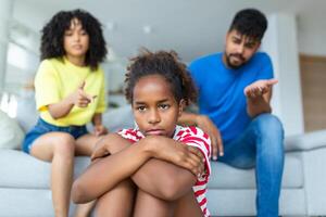 travieso niño. irritado padres regaño su pequeño hija para su comportamiento mientras sentado juntos en sofá a hogar foto