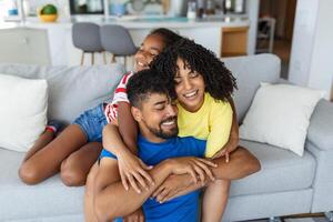 contento familia madre padre y niño hija riendo y teniendo divertido a hogar. contento africano americano familia relajante foto