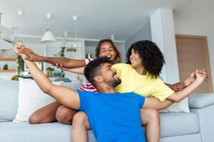 linda africano americano familia disfrutando hora juntos. contento padres sonriente mientras sentado en sofá con adorable hija foto