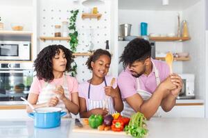 alegre joven padres y pequeño hija teniendo divertido mientras horneando juntos en cocina, contento africano americano familia canto y engañando, utilizando espátula y batidor como micrófonos, Copiar espacio foto