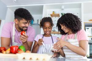 Disparo de hermosa linda familia teniendo divertido mientras Cocinando juntos en el cocina a hogar. linda pequeño niña y su hermosa padres son sonriente mientras Cocinando en cocina a hogar foto