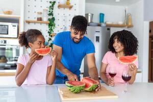 Dad is cutting watermelon while mom and daughter are watching him. photo