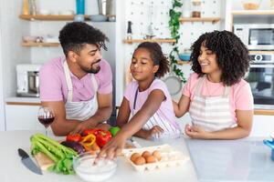 Happy family cooking together on kitchen. Mother and daughter with fathe cooking. Dad and daughter chopping green vegetable leaf for salad. Home recreation and food preparation on weekend photo