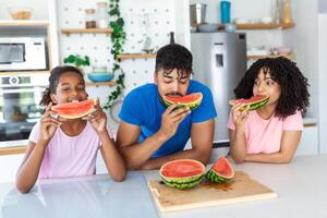 Family eats a sweet watermelon in the kitchen. A man and a woman with daughter eat a ripe watermelon in the kitchen. Happy family eating watermelon. photo