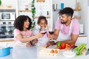 Shot of beautiful cute family having fun while cooking together in the kitchen at home. Cute little girl and her beautiful parents are smiling while cooking in kitchen at home photo