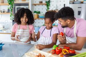 Happy family cooking together on kitchen. Mother and daughter with father cooking. Dad and daughter chopping green vegetable leaf for salad. Home recreation and food preparation on weekend photo