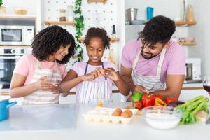 contento amoroso familia son preparando panadería juntos. madre, padre y niño hija niña son Cocinando galletas y teniendo divertido en el cocina. hecho en casa comida y pequeño ayudante. foto