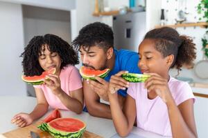 Young Family eating watermelon and having fun. Mixed race family in kitchen together eating a watermelon slice. photo