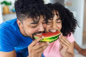 A couple in love eats a sweet watermelon in the kitchen. A man and a woman eat a ripe watermelon in the kitchen. Happy couple eating watermelon. Portrait of a couple with a watermelon photo
