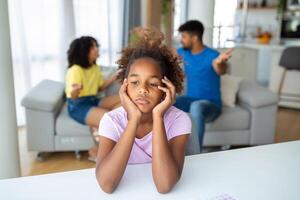 Divorce And Domestic Violence. Portrait of upset African American daughter looking through the window while her angry parents fighting in the background, depressed child feeling lonely photo