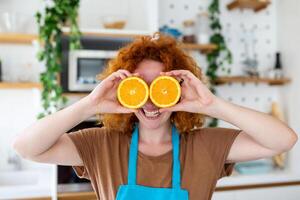 foto de linda caucásico mujer sonriente y participación dos naranja partes mientras Cocinando vegetal ensalada en cocina interior a hogar