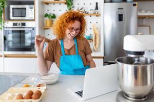 un joven mujer aprende a cocinar, ella relojes vídeo recetas en un ordenador portátil en el cocina y cocinar un plato . Cocinando a hogar concepto foto