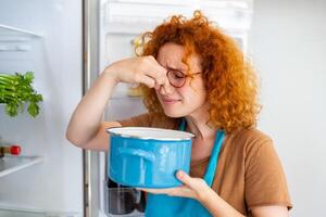 malo comida en refrigerador, joven mujer en participación su nariz porque de malo oler desde comida en refrigerador a hogar foto