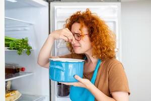 malo comida en refrigerador, joven mujer en participación su nariz porque de malo oler desde comida en refrigerador a hogar foto