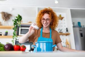 Cute young woman cooking and adding spice to meal, laughing and spending time in the kitchen photo