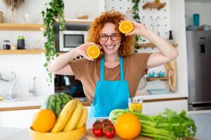 foto de linda caucásico mujer sonriente y participación dos naranja partes mientras Cocinando vegetal ensalada en cocina interior a hogar