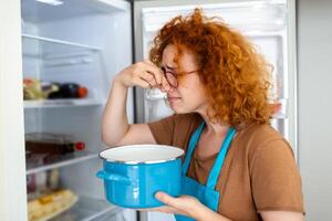 malo comida en refrigerador, joven mujer en participación su nariz porque de malo oler desde comida en refrigerador a hogar foto