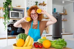 foto de linda caucásico mujer sonriente y participación dos naranja partes mientras Cocinando vegetal ensalada en cocina interior a hogar