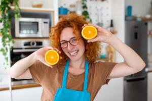 foto de linda caucásico mujer sonriente y participación dos naranja partes mientras Cocinando vegetal ensalada en cocina interior a hogar