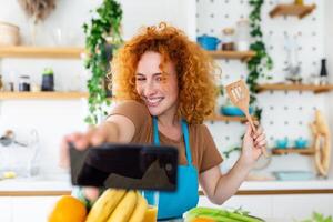 Young woman is in the kitchen, she has wireless headphones on, she is dancing and singing photo