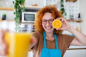 foto de linda caucásico mujer sonriente y participación dos naranja partes mientras Cocinando vegetal ensalada en cocina interior a hogar