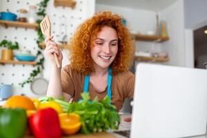 A young woman learns to cook, she watches video recipes on a laptop in the kitchen and cook a dish . Cooking at home concept photo