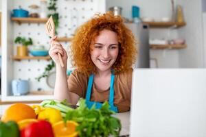 A young woman learns to cook, she watches video recipes on a laptop in the kitchen and cook a dish . Cooking at home concept photo