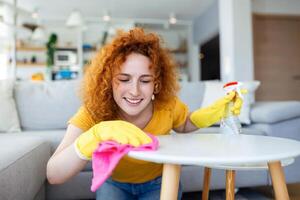 Beautiful young woman cleaning the house. Girl rubs dust. Smiling woman wearing rubber protective yellow gloves cleaning with rag and spray bottle detergent. Home, housekeeping concept. photo