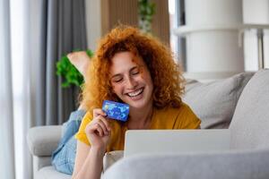 Female consumer spending buying on internet, lifestyle. Happy woman shopping online with laptop at home. Woman using laptop computer shopping on line, using credit card playing online, smiling indoors photo