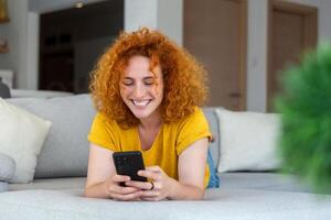Woman using mobile phone while lying on sofa. Young female is resting at home. photo