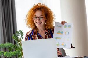 Focused business woman presenting charts and graphs on video call online. Young business woman having conference call with client on laptop. Young woman explaining how business work photo