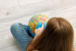 girl sitting on the floor unwinds the globe pointing her finger at India photo