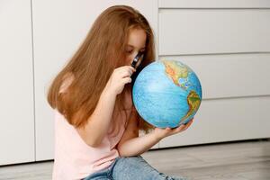 niña sentado en el piso cuidadosamente estudiando el globo con un aumentador vaso foto