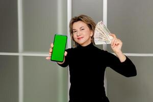 contento mujer con dinero en manos y teléfono con verde pantalla, banca de lista de tiro, foto