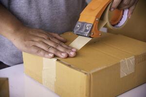 The staff is using the tape to pack the package goods to the customer. photo