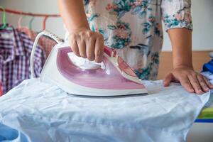 cerca arriba de mujer planchado ropa en planchado tablero foto