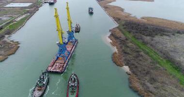 Towing cranes for containers. Large container ship pulled by tugboats. Top down aerial view. Container Cargo freight ship with working crane bridge in shipyard at dusk for Logistic Import Export video