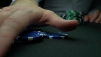 Man's hand take chips from the poker table on black background. Poker chips and hands above it on green table. Hand takes the winnings in poker in slow motion video