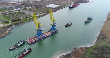 Towing cranes for containers. Large container ship pulled by tugboats. Top down aerial view. Container Cargo freight ship with working crane bridge in shipyard at dusk for Logistic Import Export video