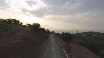 Aerial view on serpentine road with beautiful sea coast landscape with mountain background. Shot. Top view on green coastal mountain road landscape flight with haze at sunset time. video