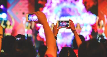 aficionados son teniendo divertido, ambos tomando imágenes con el cámara y móvil teléfono. concierto ejecutante foto