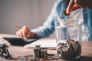 hand holding coins to put the glass piggy bank. Saving and financial accounts concept photo