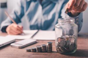 hand holding coins to put the glass piggy bank. Saving and financial accounts concept photo