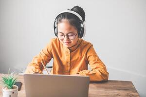 Teenage Asian students in a yellow dress wearing a headphone are communicating through video conferencing for online learning. In a video conference call via apps. new normal concept photo