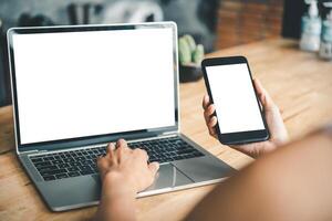 mockup image of a woman's hand working on a laptop and smart phone with blank white desktop copy space screen on a desk photo