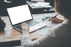 Rear view mockup image of a woman's hand working on a laptop with blank white desktop copy space screen on a desk photo