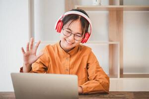 Teenage Asian students in a yellow dress wearing a headphone are communicating through video conferencing for online learning. In a video conference call via apps. new normal concept photo